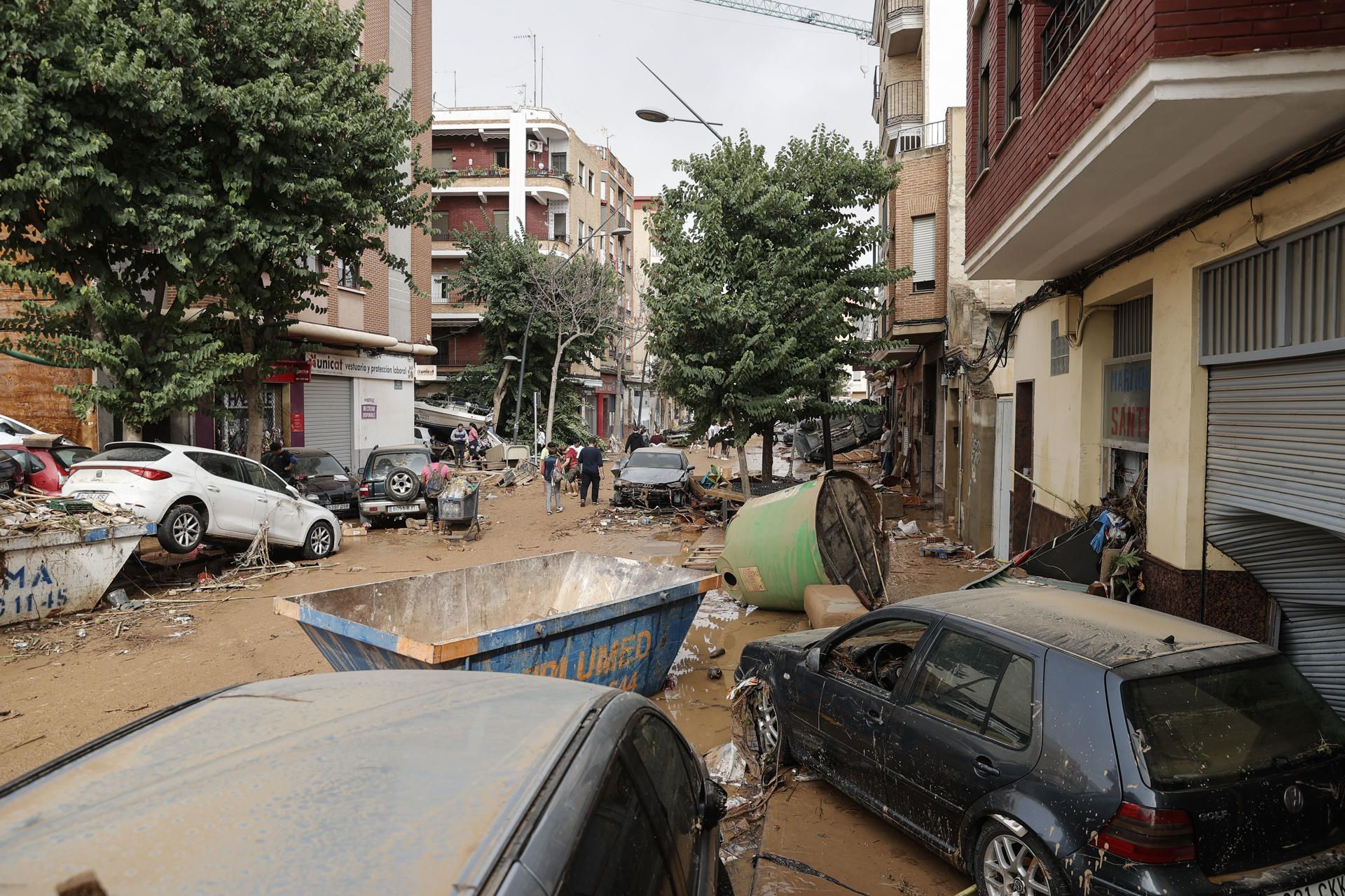 Unas personas caminan por una calle cubierta de lodo y llena de coches amontonados tras las intensas lluvias por la fuerte dana que afecta especialmente el sur y el este de la península ibérica, este miércoles en Valencia. EFE.